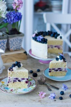 two slices of blueberry cheesecake on plates with flowers in the vases behind them