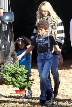 a group of people standing around a tree in front of a truck with a child on it