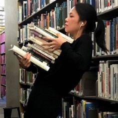 a woman is picking up some books from a book shelf in a library and listening to headphones