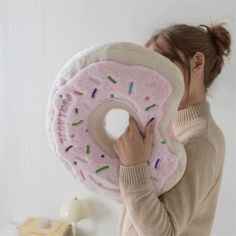 a woman holding a donut pillow with sprinkles on it