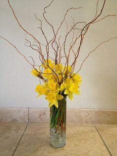 a vase filled with yellow flowers sitting on top of a tiled floor next to a wall