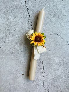 a candle with a sunflower on it sitting on the ground next to a piece of paper