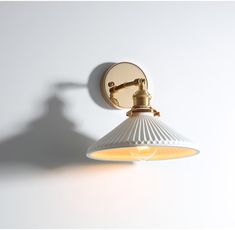 a wall light with a white shade on it's side and a shadow cast on the wall behind it