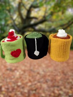 three crocheted mug cozyies hanging from a line in front of a tree