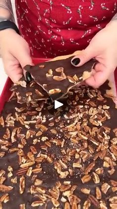 a woman is cutting into a chocolate cake with pecans on the top and nuts on the bottom