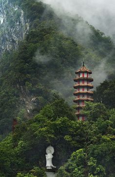 a tall tower sitting on top of a lush green forest covered hillside next to a mountain