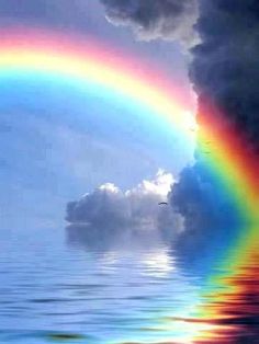 a rainbow in the sky over water with clouds