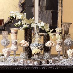 a table topped with vases filled with white flowers and candies next to each other