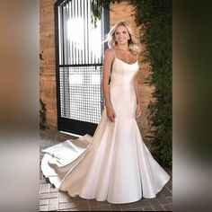 a woman in a white wedding dress posing for a photo with greenery on the wall behind her