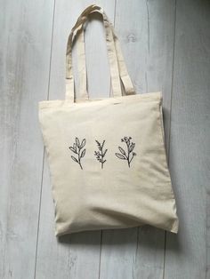 a white bag with black flowers on it sitting on top of a wooden floor next to a plant