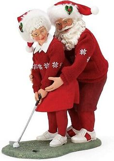 two figurines are dressed as santa and mrs claus on the green golf course