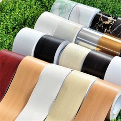 several rolls of satin ribbon sitting on top of each other in front of green bushes