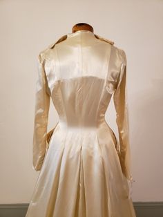 "1950s, 34\"bust,wedding ensemble consists of gown and coat of egg shell white rayon slipper satin. Gown has crystal beading at bosom, in a bow motif. Bodice of gown is strapless, with stays sewn into the interior of bodice, bodice comes to a point at waist. Skirt is full, fuller in back, and a bit longer in back than front. Coat has rounded lapels, buttons at mid section with 5 round satin buttons. Skirt of coat is floor length in front, with a cathedral length train in back. Faux pockets are a Vintage Fitted Wedding Dress For Debutante Ball, Cream Ball Gown For Evening, Regency Style Fitted Wedding Gown, Cream Satin Gown With Fitted Bodice, Victorian Dress With Boned Bodice For Weddings, Vintage Silk Gown For Formal Occasions, Vintage Satin Gown For Debutante Ball, Vintage Cream Gown For Debutante Ball, Cream Vintage Gown For Debutante Ball