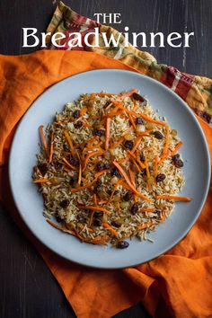 a white plate topped with rice covered in carrots and raisins next to an orange napkin