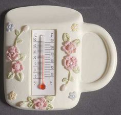 a thermometer sitting on top of a white cup with pink flowers and leaves