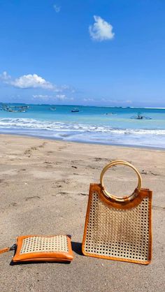 a wicker purse sitting on top of a sandy beach next to the ocean with boats in the background