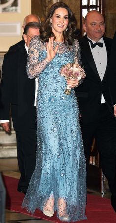 a woman in a blue dress is walking down the red carpet with her hand on her chest