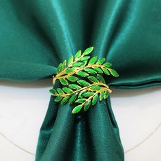 a green napkin with a gold leaf brooch on it's side, resting on a white plate