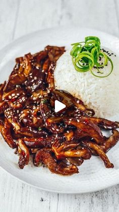 a white plate topped with rice and meat next to green garnish on top of it