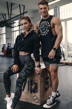 a man and woman sitting on top of a box in a gym room, posing for the camera