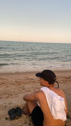 a person sitting on the beach with their feet in the sand looking at the water