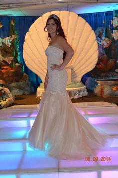 a woman in a wedding dress standing on a stage with an ocean shell behind her