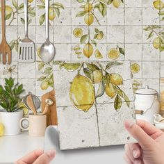 two hands are holding an object in front of a tile wall with lemons on it