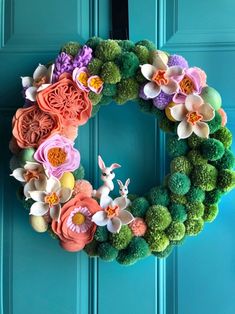 a colorful wreath with flowers and rabbits on the front door is hung on a blue door