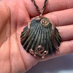 a hand holding a necklace with a seashell on it's side and spirals in the middle