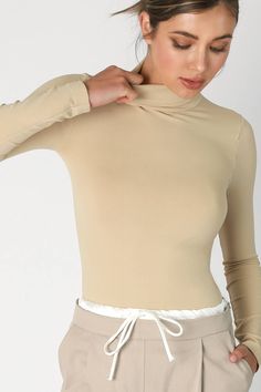 Indulge in timeless elegance with our Pearl Long Sleeve Mock Neck Top. Crafted from a luxurious blend of 92% Nylon and 8% Spandex, this seamless top is designed to provide a form-fitting look for effortless layering. Made in the USA, it serves as the perfect base layer for any ensemble, offering a cozy neckline and a sophisticated silhouette. Elevate your style with this essential piece from our premium collection. Elegant High Stretch Tops With Thumbholes, Stretch Long Sleeve Tops With Seamless Collar, Winter Athleisure Fitted Tops, Elastane Turtleneck Top, Fitted High Neck Beige Tops, Fitted High Neck Tops For Athleisure, Beige Fitted High Neck Top, Elastane Tops With Thumbholes, High Stretch Elastane Tops With Seamless Construction