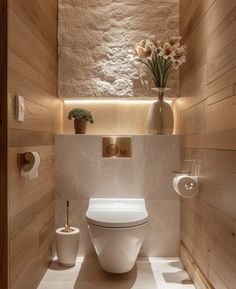 a white toilet sitting inside of a bathroom next to a vase with flowers on it