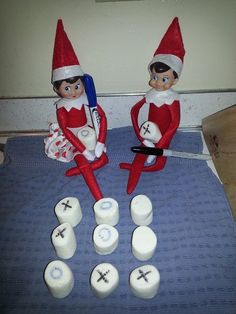 two elfs sitting on top of a bed next to some dice and toothpaste