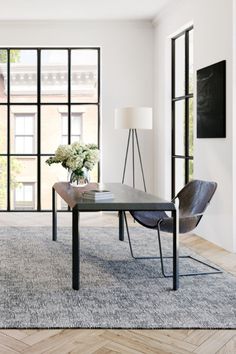 a living room with large windows and a table in front of the window on top of a rug