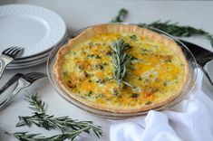 a quiche with cheese and herbs in a pie pan on a table next to silverware