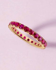 a yellow gold ring with pink stones on the inside and outside, set against a light purple background