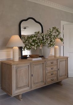 a wooden dresser with two lamps and a mirror on it's sideboard in a living room