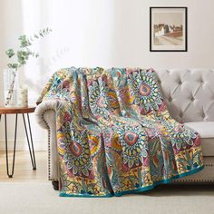 a couch with a colorful blanket on top of it next to a table and potted plant