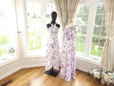 two dresses on mannequins in front of windows with curtains and flowered drapes