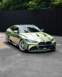 a green sports car parked in a parking lot next to a black fence and trees