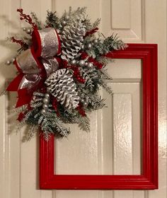 a red frame holding a wreath with silver pineconis and bells on the front door