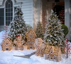 christmas trees and gingerbread houses are decorated with lights in front of a white house