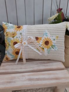 a sunflower pillow on a wooden bench with flowers in the background and a ribbon tied around it