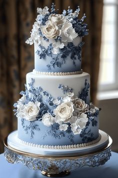 a three tiered blue and white wedding cake with flowers on the top is sitting on a table