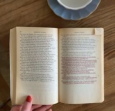 an open book sitting on top of a wooden table next to a cup of coffee