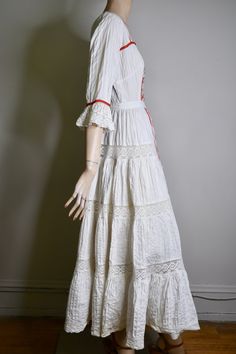 "This dress is so special. It is a vintage 60s/70s Mexican pin tucked white dress. The dress has a square neckline, that is trimmed with red ribbon and small lace ruffles, is fitted to the waist with a floral embroidered bodice that is also finished on the side with red ribbon, it has 3/4 sleeves with a flared lace cuff and red ribbon trim, The skirt is a long maxi skirt that is quite full, it has a front and back center panel with red ribbon running down the length, coming off the front panel i Bohemian Lace Dress With Broderie Anglaise, White Folk Style Wedding Dress, White Lace Trim Maxi Dress For Festivals, Fitted Broderie Anglaise Maxi Dress, Fitted White Maxi Dress For Festival, White Fitted Maxi Dress For Festival, Bohemian Cotton Dresses With Broderie Anglaise, Fitted Lace Trim Maxi Dress For Festivals, Fitted Festival Maxi Dress With Lace Trim