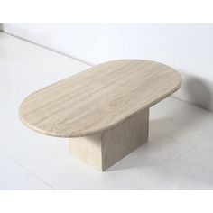 an oval stone table sitting in the middle of a white floored room with a wall behind it