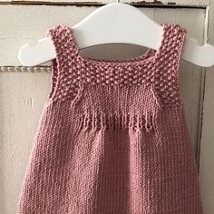 a pink knitted baby dress hanging on a white hanger next to a door