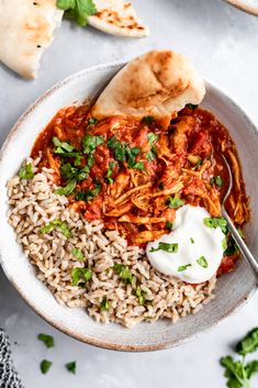 a bowl filled with rice, meat and sauce next to pita bread on the side