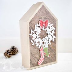 a card with a christmas wreath and stockings hanging from it's side, next to pine cones