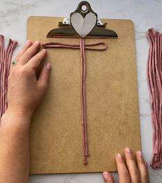 someone is making a paper heart decoration on a clipboard with pink yarn and scissors